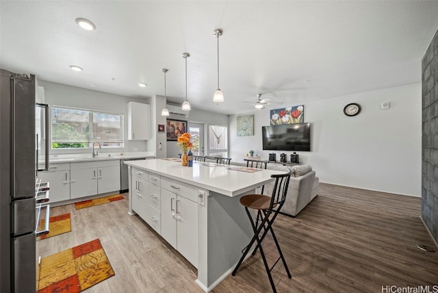 kitchen featuring stainless steel appliances, a center island, pendant lighting, white cabinets, and light hardwood / wood-style floors