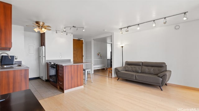 kitchen with black electric range, sink, a kitchen breakfast bar, light hardwood / wood-style floors, and white fridge