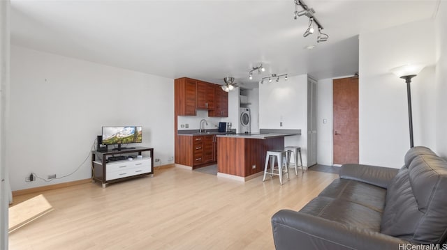 living room with sink, light hardwood / wood-style floors, ceiling fan, stacked washer and dryer, and track lighting