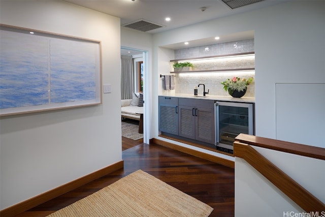 bar featuring dark wood-type flooring, decorative backsplash, sink, and beverage cooler