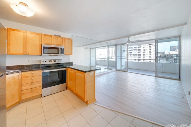 kitchen featuring dark stone counters, kitchen peninsula, appliances with stainless steel finishes, and light hardwood / wood-style flooring