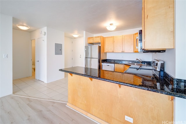 kitchen with dark stone countertops, light hardwood / wood-style floors, a kitchen bar, kitchen peninsula, and stainless steel appliances