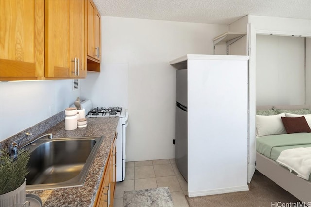 kitchen with sink, light tile patterned floors, stainless steel refrigerator, a textured ceiling, and white range with gas cooktop