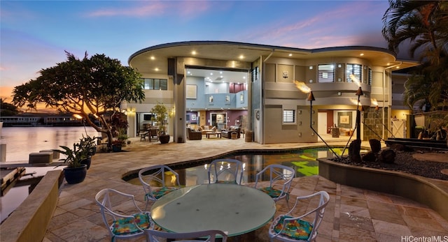 back house at dusk featuring a water view and a patio area