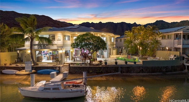 back house at dusk with a water and mountain view, a patio, and a swimming pool