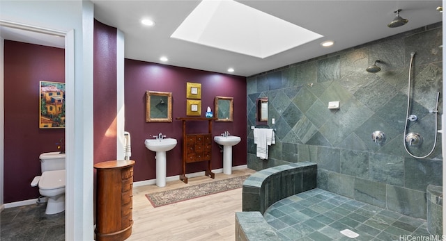 bathroom featuring tiled shower, wood-type flooring, toilet, sink, and a skylight