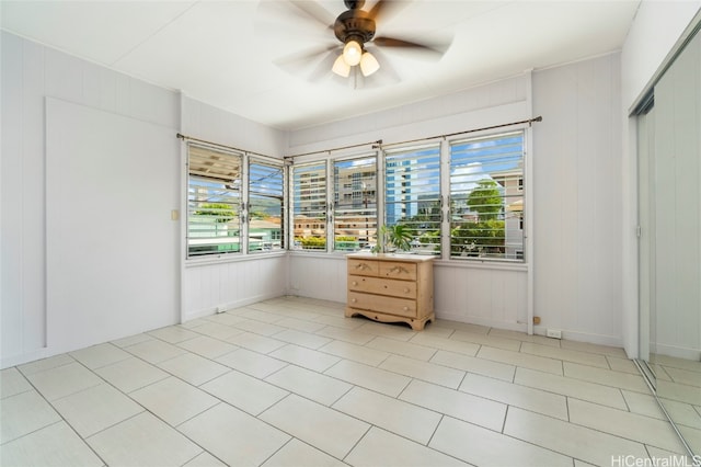 unfurnished bedroom with a closet, wooden walls, light tile patterned flooring, and ceiling fan