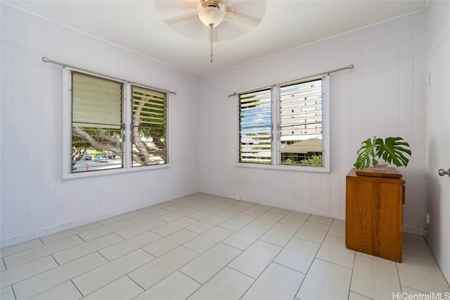 tiled empty room featuring wood walls, a healthy amount of sunlight, and ceiling fan