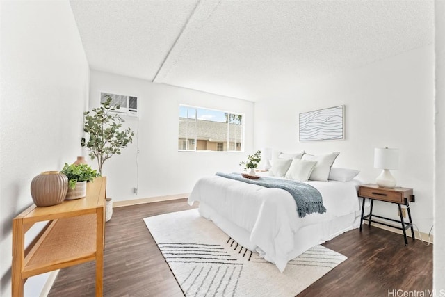 bedroom with baseboards, dark wood finished floors, a textured ceiling, and a wall mounted AC