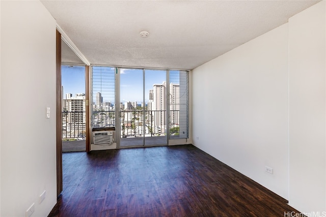 unfurnished room featuring a wall of windows, a textured ceiling, plenty of natural light, and dark hardwood / wood-style flooring