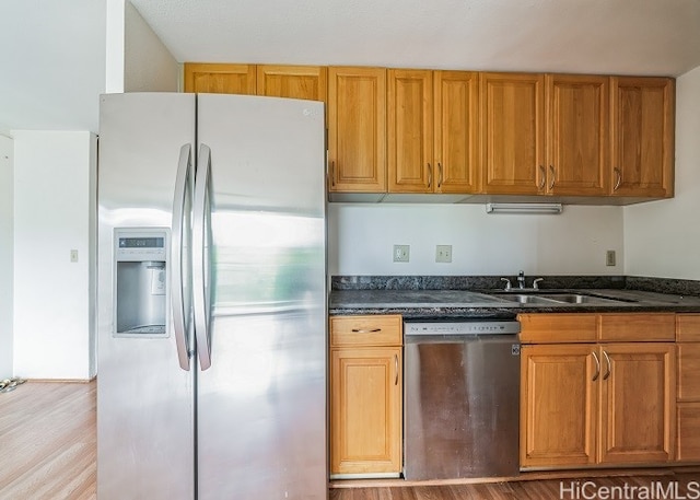 kitchen featuring dark stone countertops, stainless steel appliances, light hardwood / wood-style flooring, and sink