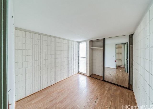 unfurnished bedroom with tile walls, hardwood / wood-style floors, and a closet