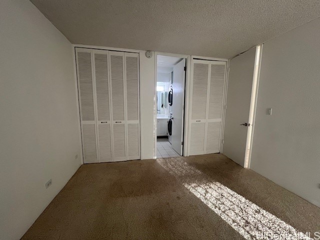 unfurnished bedroom with a textured ceiling, ensuite bath, light colored carpet, and two closets