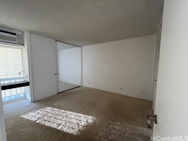 spare room with a textured ceiling, carpet floors, and a wall mounted air conditioner