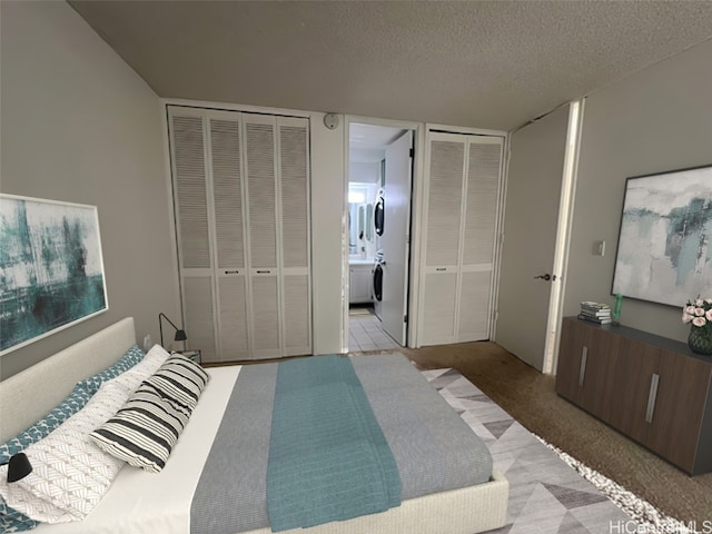 carpeted bedroom with washer / clothes dryer, two closets, a textured ceiling, and ensuite bath