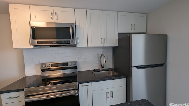 kitchen featuring appliances with stainless steel finishes, sink, backsplash, white cabinetry, and dark stone countertops