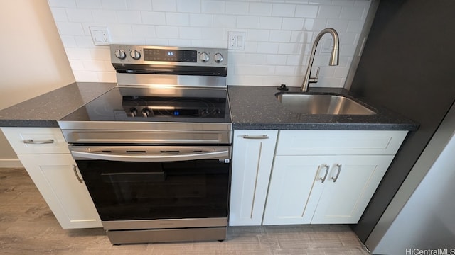 kitchen featuring sink, electric stove, backsplash, white cabinetry, and dark stone counters