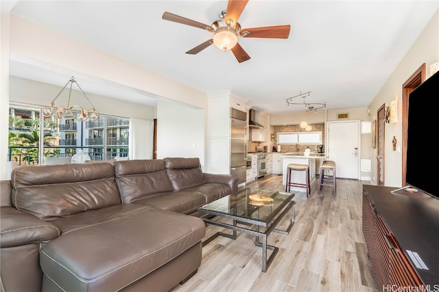 living room featuring light hardwood / wood-style floors, ceiling fan with notable chandelier, and rail lighting