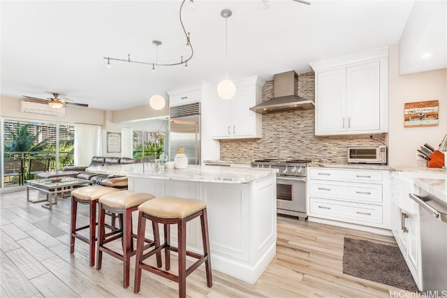 kitchen featuring wall chimney exhaust hood, a center island, premium appliances, white cabinets, and light hardwood / wood-style floors