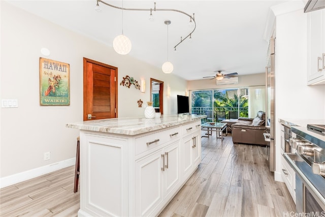 kitchen featuring hanging light fixtures, a center island, light wood-type flooring, white cabinets, and light stone counters