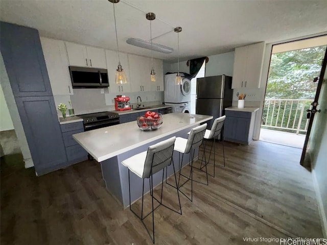 kitchen with dark wood-type flooring, stacked washer / drying machine, white cabinetry, pendant lighting, and stainless steel appliances