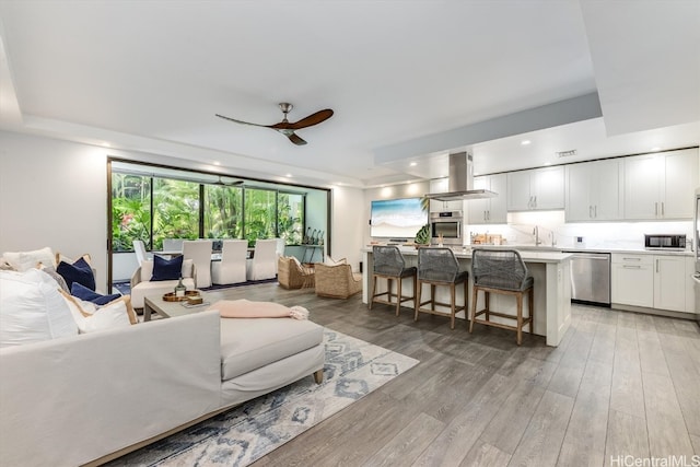 living room with sink, a tray ceiling, light wood-type flooring, and ceiling fan