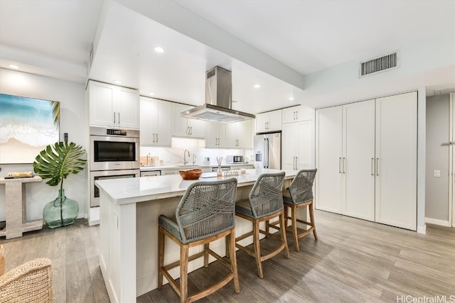 kitchen featuring light hardwood / wood-style flooring, white cabinetry, stainless steel appliances, and a center island with sink