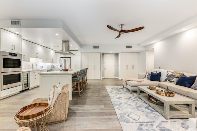 living room with sink, ceiling fan, light hardwood / wood-style flooring, and beverage cooler