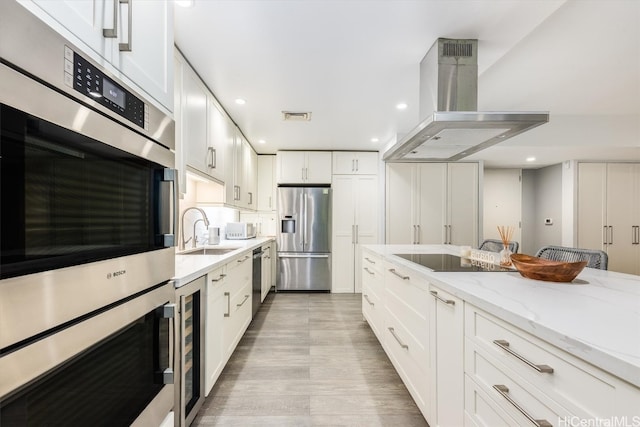 kitchen featuring appliances with stainless steel finishes, sink, island range hood, white cabinetry, and light stone counters