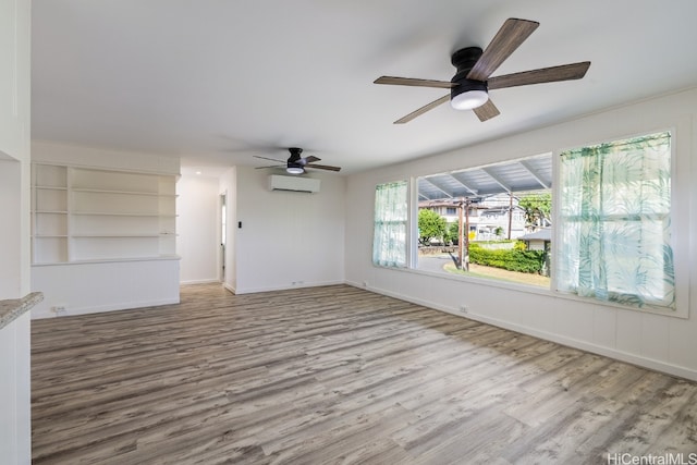 unfurnished living room featuring built in shelves, ceiling fan, a wall mounted AC, and light hardwood / wood-style flooring