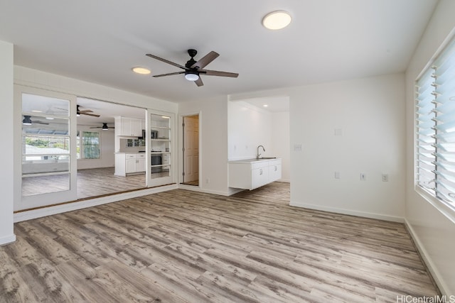 empty room with light wood-style flooring, baseboards, ceiling fan, and a sink