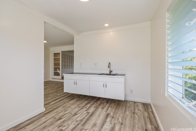 interior space with light wood-type flooring, white cabinetry, baseboards, and a sink