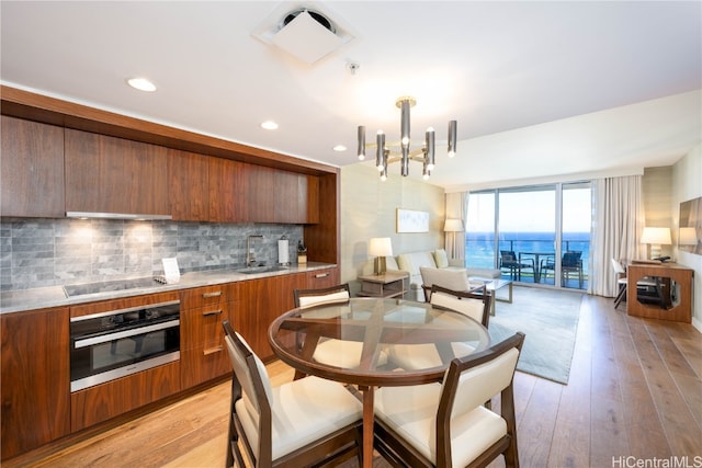 kitchen with black electric stovetop, backsplash, oven, and light wood-type flooring