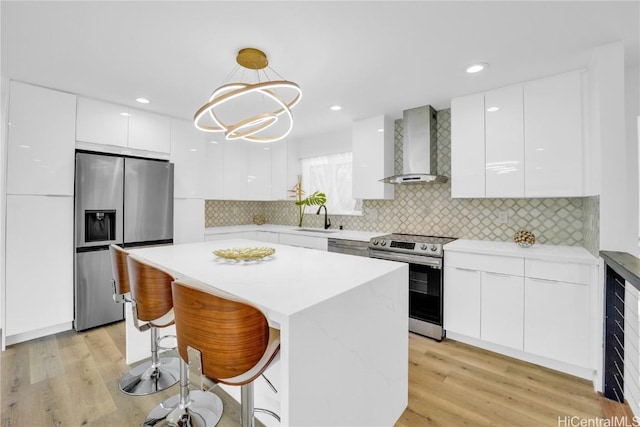 kitchen featuring wall chimney range hood, appliances with stainless steel finishes, tasteful backsplash, white cabinets, and decorative light fixtures