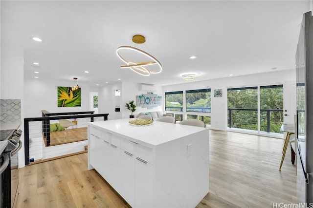 kitchen with decorative light fixtures, light hardwood / wood-style flooring, a kitchen island, range with electric cooktop, and white cabinets