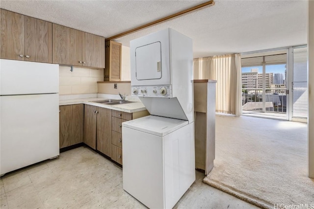 laundry area featuring a textured ceiling, stacked washing maching and dryer, and sink