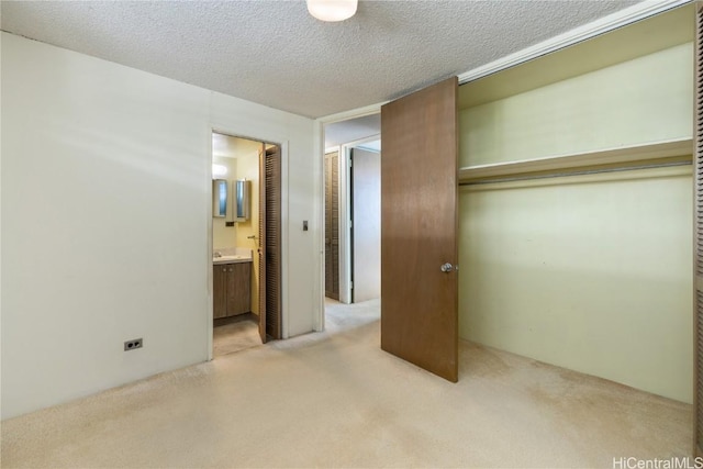 unfurnished bedroom with light colored carpet, a textured ceiling, connected bathroom, and a closet