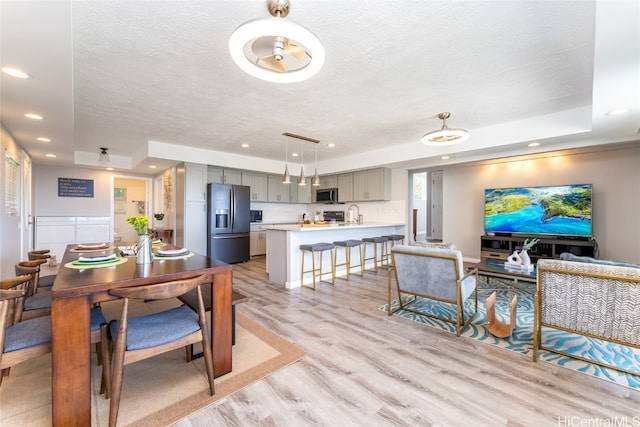 dining area with a textured ceiling, a tray ceiling, and light wood-type flooring