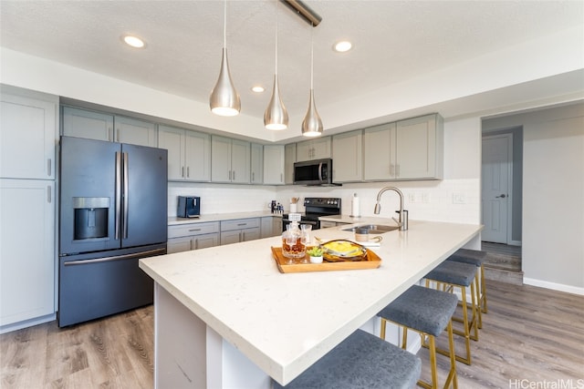 kitchen featuring hanging light fixtures, appliances with stainless steel finishes, a textured ceiling, light hardwood / wood-style flooring, and sink