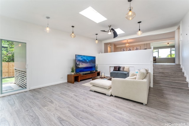 living room featuring ceiling fan, a skylight, and light hardwood / wood-style flooring