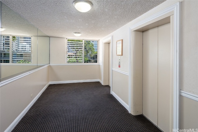 hallway with elevator, a textured ceiling, and dark colored carpet