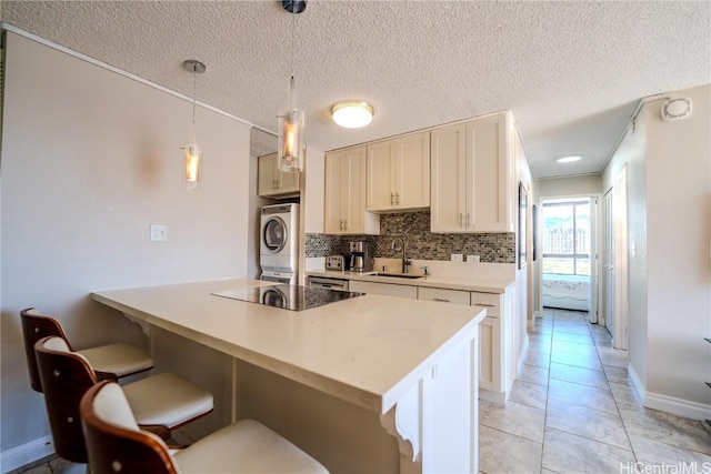 kitchen with black electric stovetop, decorative light fixtures, stacked washing maching and dryer, a breakfast bar, and sink