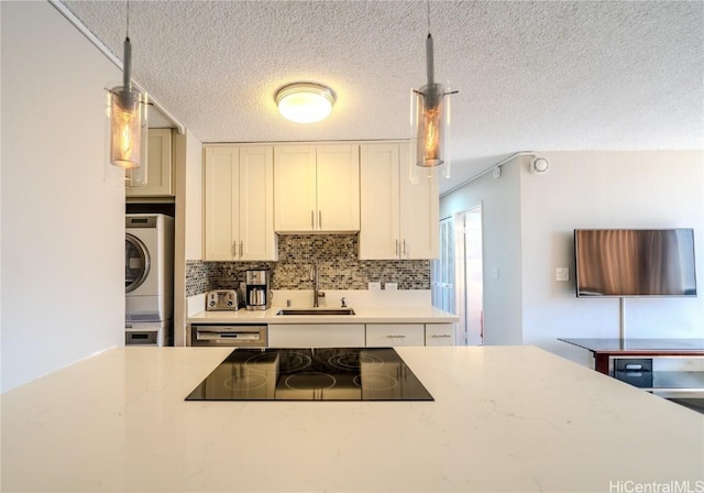 kitchen with sink, hanging light fixtures, stacked washer / dryer, white cabinets, and black electric cooktop