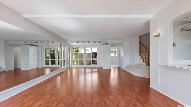 unfurnished living room featuring baseboards, rail lighting, wood finished floors, and stairway