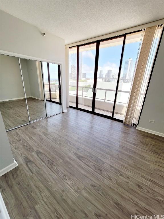 unfurnished bedroom with a wall of windows, a textured ceiling, dark hardwood / wood-style flooring, access to outside, and a closet