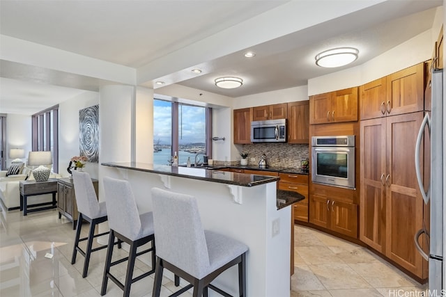 kitchen with a breakfast bar area, stainless steel appliances, dark stone counters, a water view, and tasteful backsplash