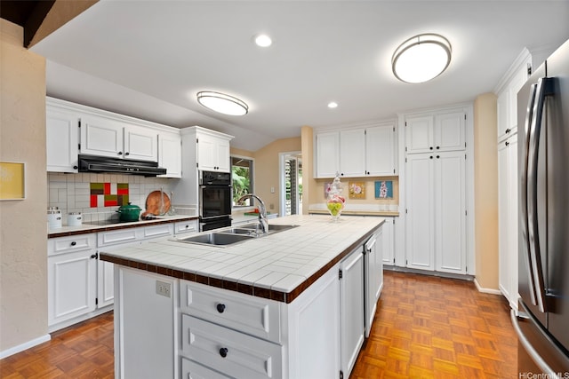 kitchen with white cabinetry, decorative backsplash, under cabinet range hood, tile countertops, and black appliances