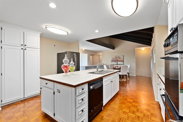 kitchen with tile counters, a sink, a center island with sink, black appliances, and white cabinetry