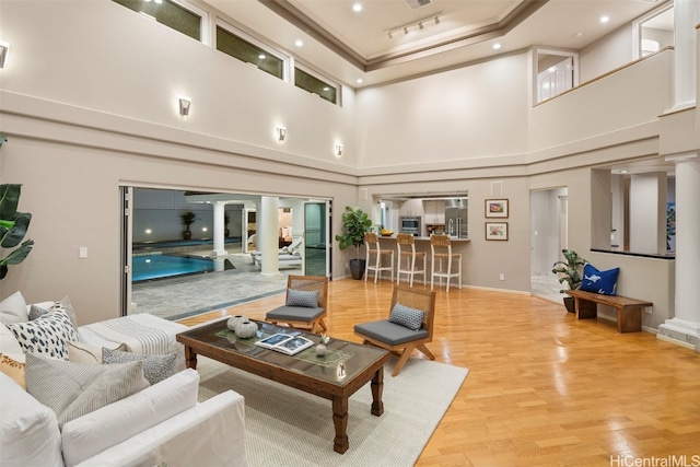 living room featuring ornate columns, a towering ceiling, and wood-type flooring