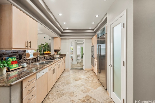 kitchen featuring tasteful backsplash, light brown cabinetry, white dishwasher, built in fridge, and dark stone counters